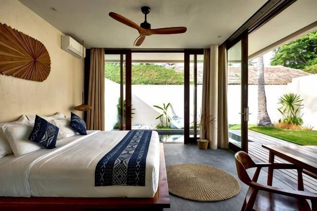 Ein Schlafzimmer mit Bett, Deckenventilator, Blick ins Freie und einem Fenster.