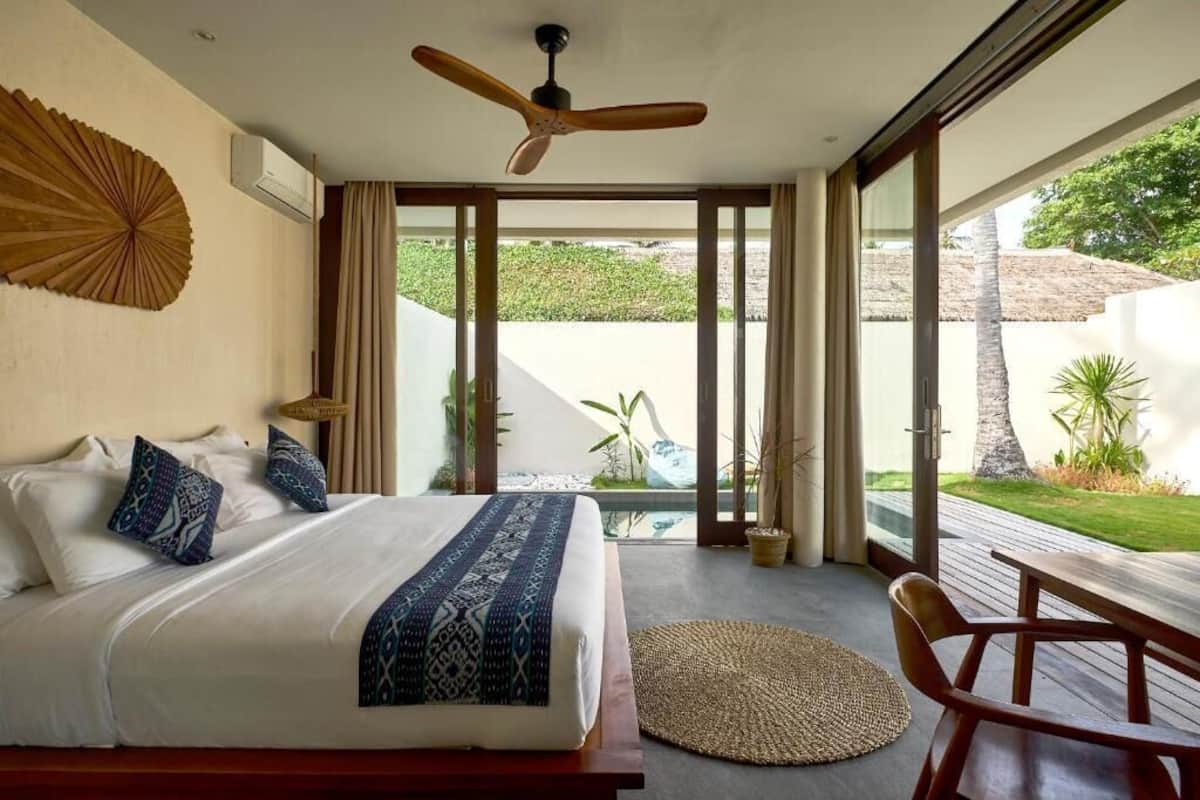 Ein Schlafzimmer mit Bett, Deckenventilator, Blick auf den Garten und einem Essbereich.