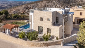 A modern stone building with a pool, surrounded by a stone wall and greenery. - 3-bdr Villa With Stunning Infinity Pool (Peristerona)