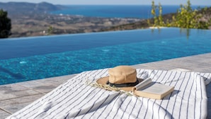 A poolside area with a hat, book, and straw on a striped towel. - 3-bdr Villa With Stunning Infinity Pool (Peristerona)