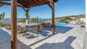 A covered outdoor area with a pool, lounge chairs, and a table with chairs. - 3-bdr Villa With Stunning Infinity Pool (Peristerona)