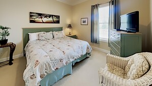 A bedroom with a bed, a television on a dresser, a chair, a lamp, and a picture on the wall.