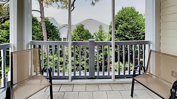 A covered porch with two chairs, a white railing, and a view of houses and trees.