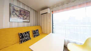 A yellow sofa with black and white pillows, a white table, and a yellow chair in a room with striped walls and a city view. - La Krasse Skytree (Tokyo)