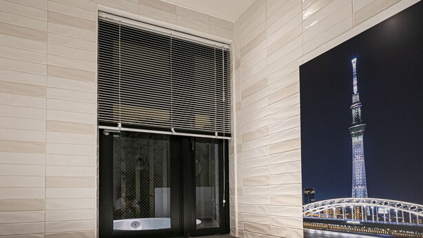 A modern bathroom with a large bathtub, a window with blinds, and a wall-mounted toilet. - La Krasse Skytree (Tokyo)