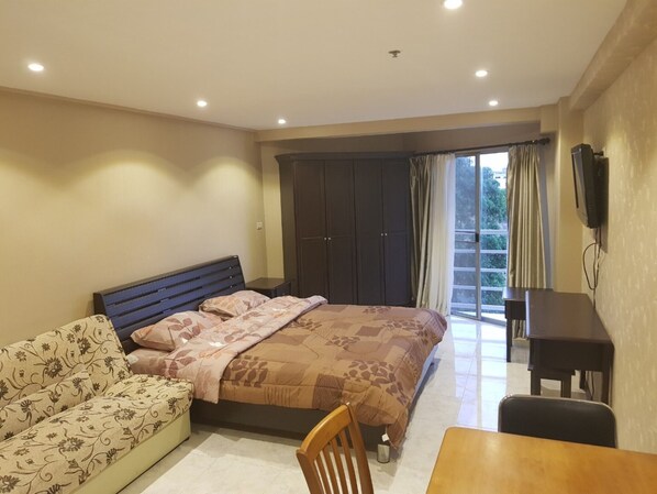 A bedroom with a bed, a sofa, a table, and a TV.