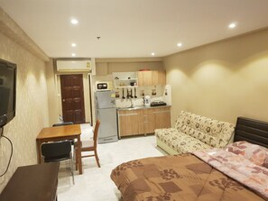 A compact hotel room with a bed, a sofa, a dining table, and a kitchenette.