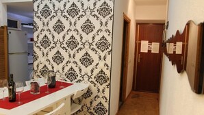 A narrow hallway with a patterned wallpaper, a wooden door with papers, and a white table with wine glasses and a bottle. - Apartment in front of Plaza Mayor and Sol (Madrid)