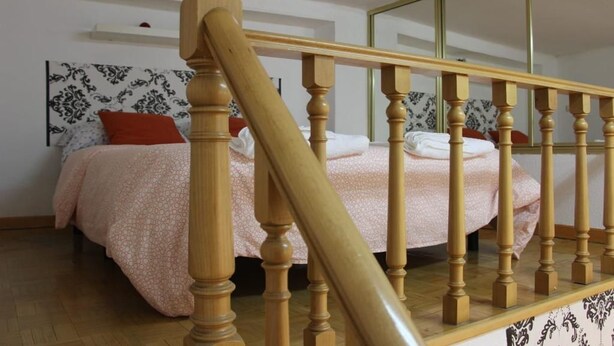 A bedroom with a wooden staircase, a bed with a patterned bedspread, and a mirror on the wall. - Apartment in front of Plaza Mayor and Sol (Madrid)