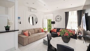 Ein modernes Wohnzimmer mit einer Couch, einem Esstisch mit Stühlen, einem großen Spiegel und einer Wanduhr.