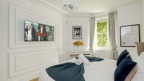 Ein Hotelzimmer mit Bett, einem an der Wand befestigten Fernseher, einem Fenster mit Vorhängen und einer gerahmten Karte an der Wand.