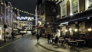 Eine Straße gesäumt von Gebäuden, einige mit Außenbestuhlung und Hinweisen zu Restaurants.