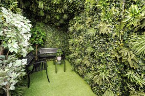 A garden area with a bench and table, surrounded by dense foliage.
