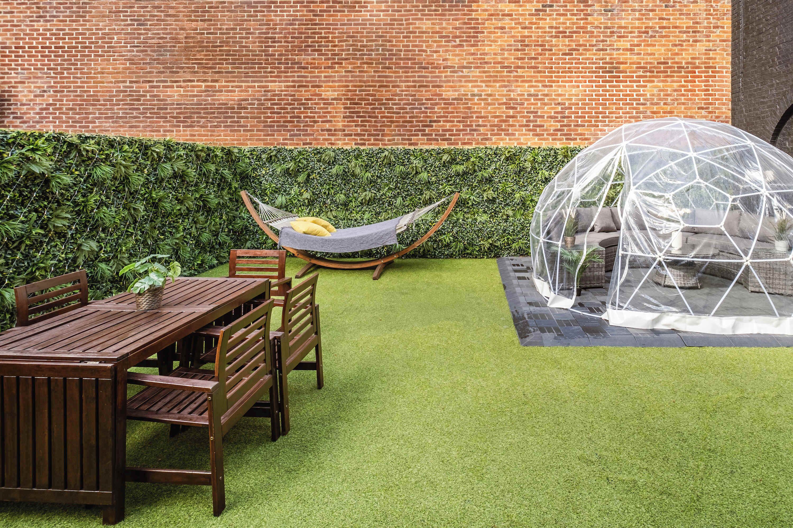 A wooden table and chairs set on artificial grass, a hammock, and a geodesic dome structure.