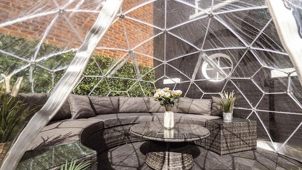 Een terras met een ronde tafel, comfortabele zitplaatsen en potplanten.