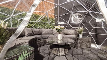 Un espace extérieur aménagé avec une table ronde, des sièges rembourrés et des plantes en pot.
