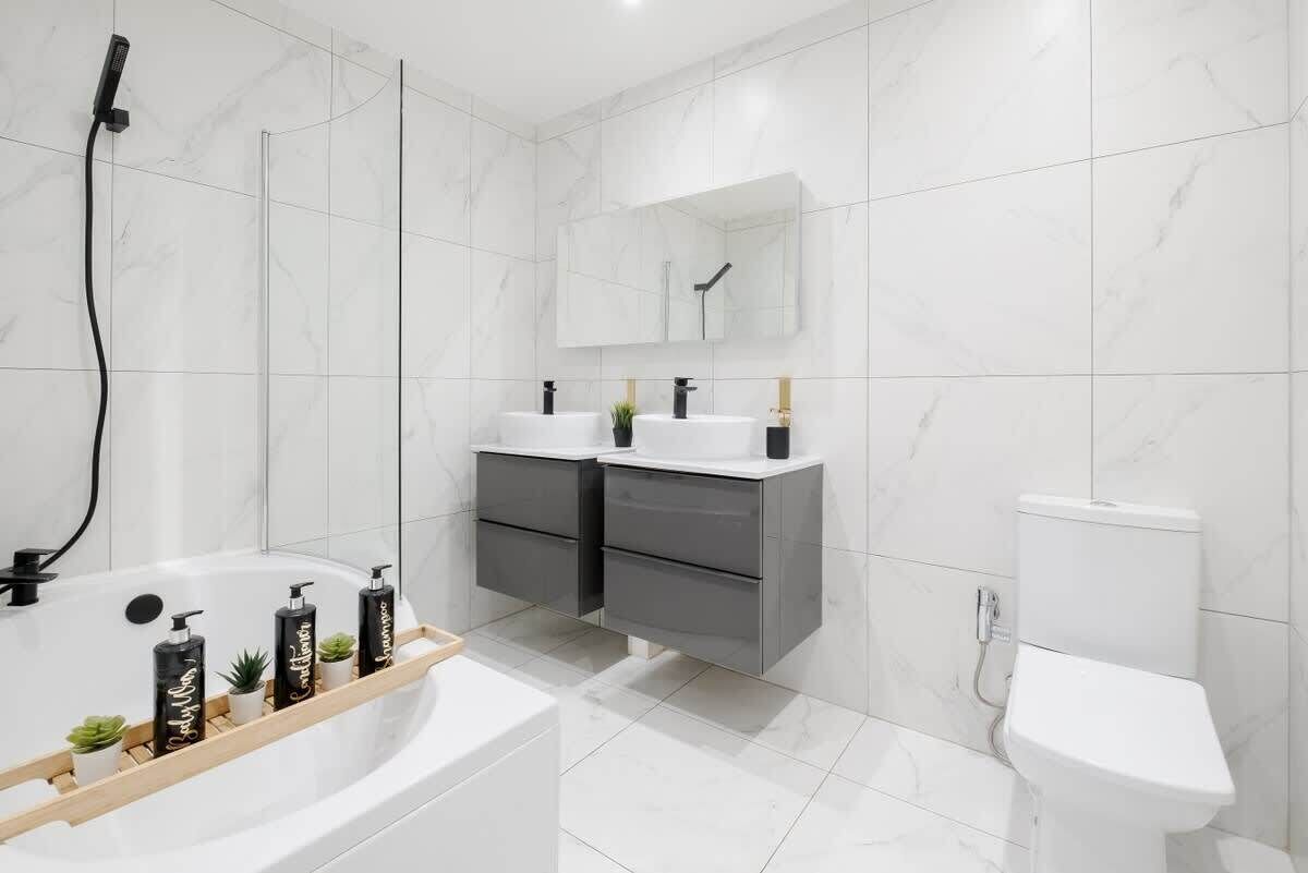 Une salle de bain moderne équipée d’une baignoire, de deux lavabos, de toilettes et d’une douche.