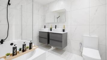 Une salle de bain moderne équipée d’une baignoire, de deux lavabos, de toilettes et d’une douche.