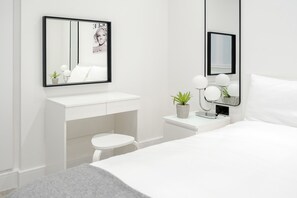 Quarto moderno e minimalista com uma toucador branca, um banquinho redondo, uma cama e um espelho grande.