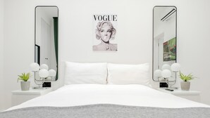 Een moderne slaapkamer met een groot bed, twee nachtkastjes met lampen, een spiegel en een aan de muur bevestigd fotolijstje.