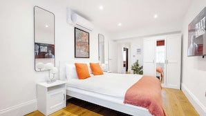 Um quarto moderno com uma cama grande, paredes brancas e chão de madeira.