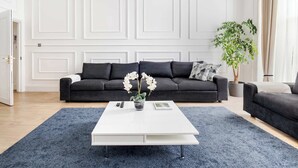 A modern living room with a dark grey sofa, a white coffee table, and a blue rug.
