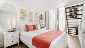 A modern bedroom with a large bed, a nightstand with drawers, a round mirror, and decorative wall art.