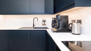 A modern kitchen with dark cabinets, a stainless steel sink, a coffee maker, and a kettle.