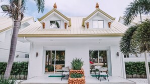 Una casa moderna con fachada blanca, dos ventanas visibles y un porche cubierto con mobiliario exterior.