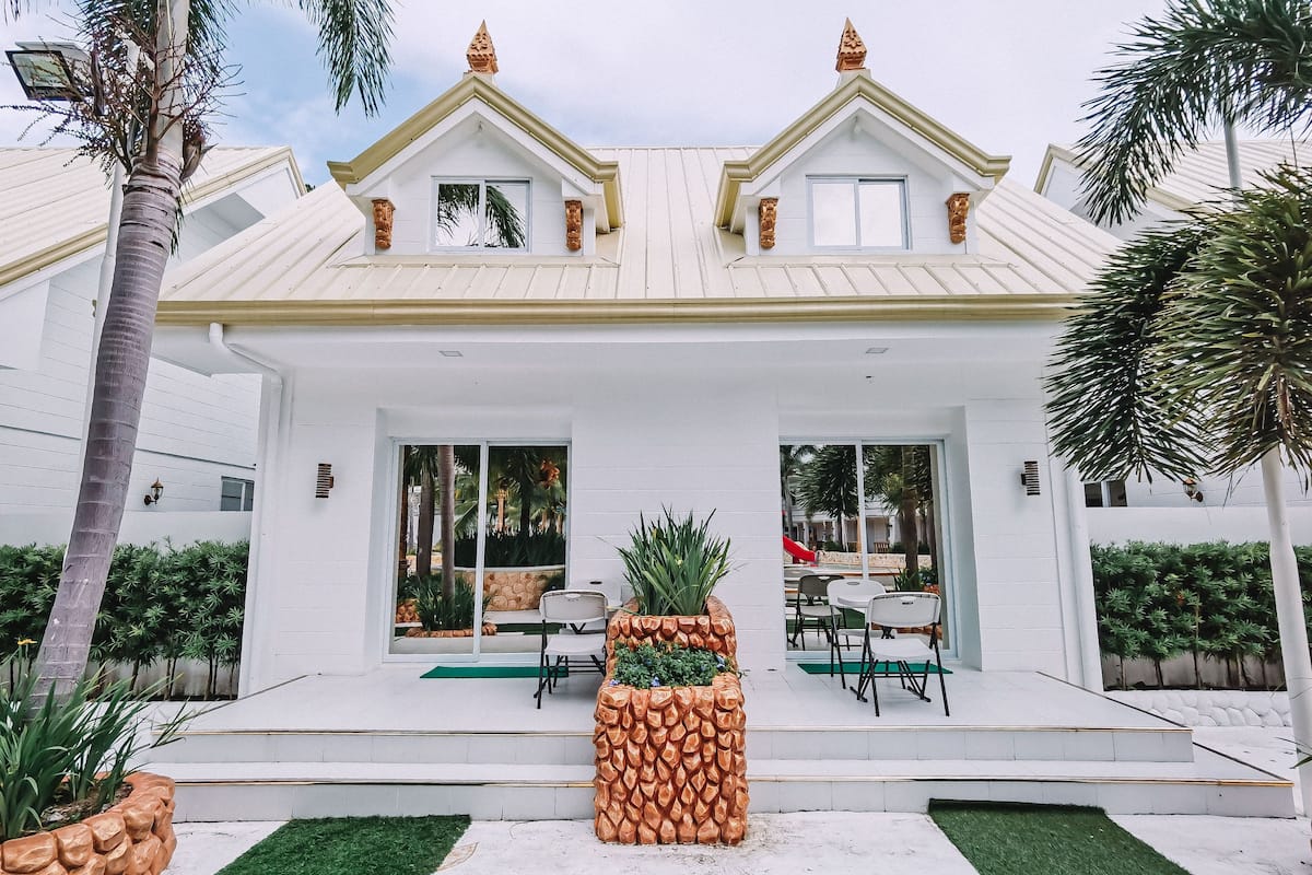 A modern house with a white exterior, two visible windows, and a covered patio area with outdoor furniture.