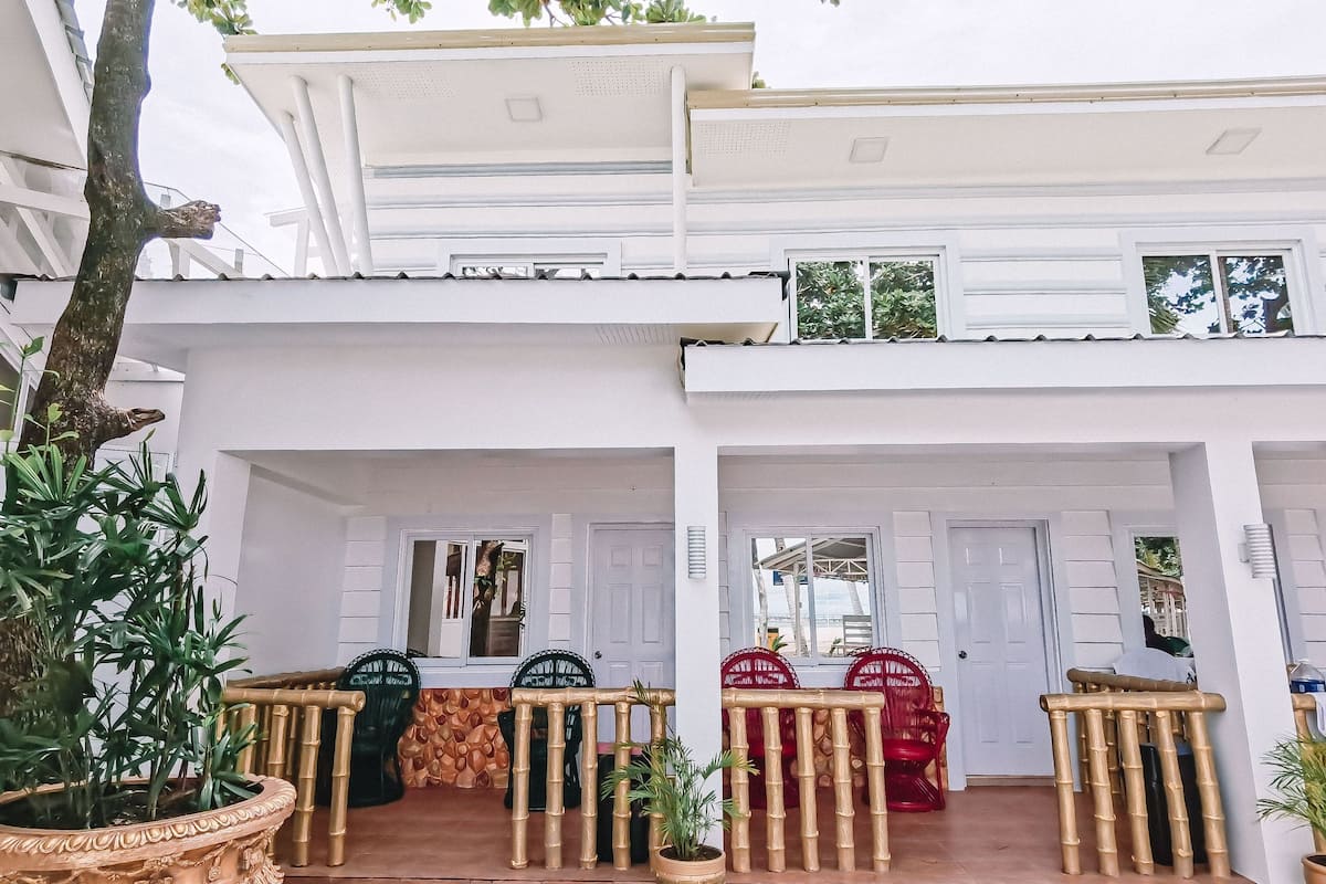 A two-story building with a covered patio area. There are potted plants and outdoor furniture.