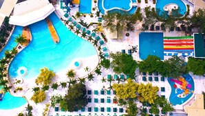 An aerial view of a resort with multiple swimming pools, palm trees, and sun loungers. - Villa Excellance Beach & Wavepool Resort (Tanza)