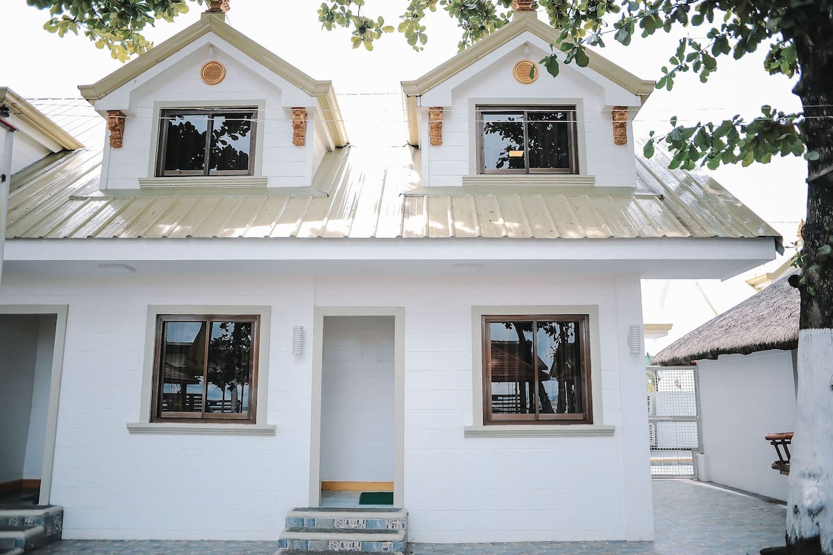 A white building with a symmetrical facade, two windows on the upper level, and a small porch with steps.