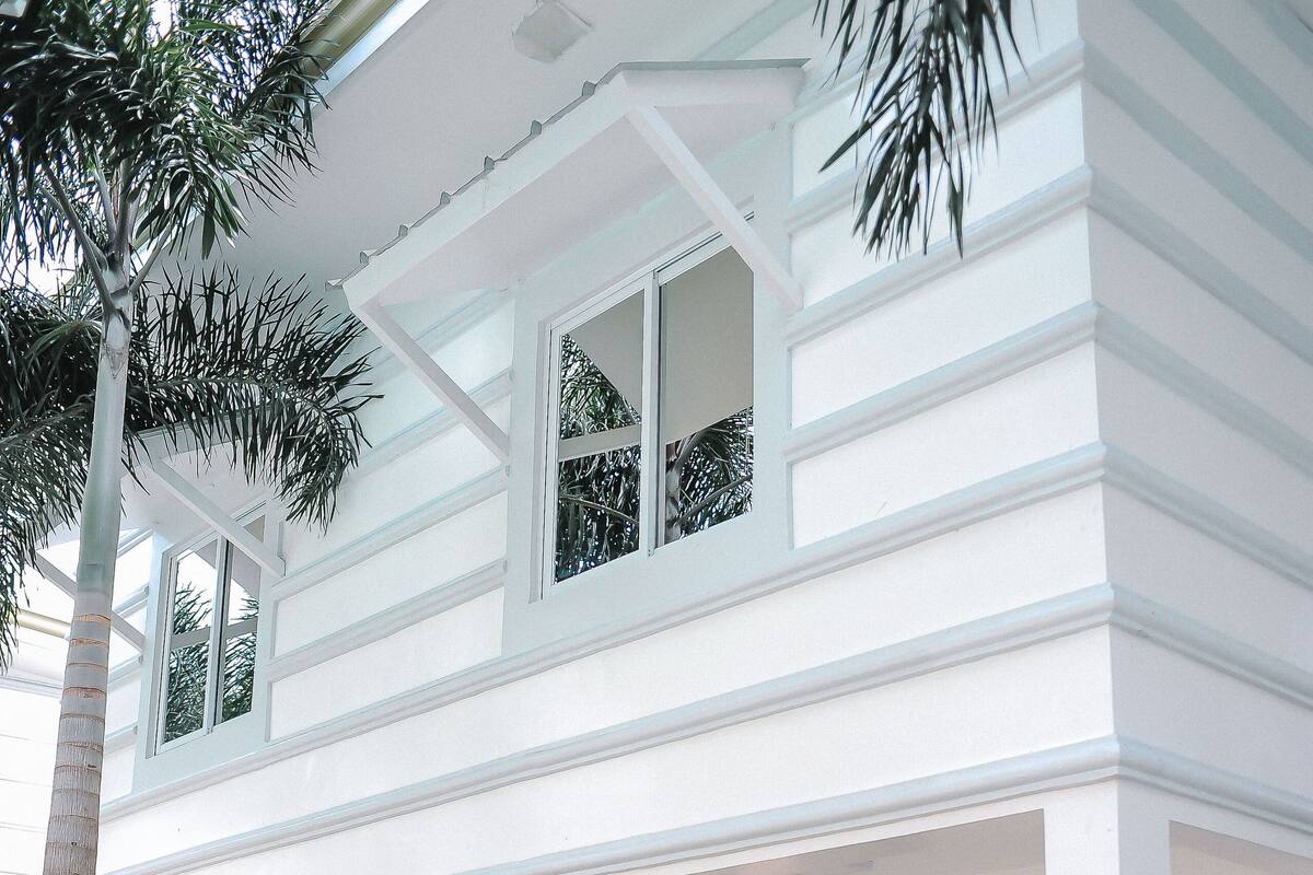 A two-story white building with a covered porch, outdoor seating, and a view of the surrounding greenery.