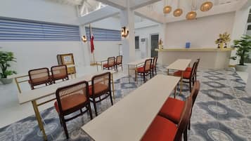 A modern dining area with high ceilings, exposed beams, and hanging wicker lamps. Tables and chairs are arranged for dining.
