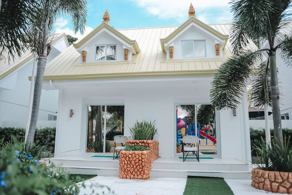 A modern house with a white exterior, a covered patio with chairs, and a visible slide in the background.
