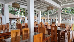 Un amplio comedor interior con mesas y sillas de madera, ventanas grandes y lámparas de mimbre colgantes.