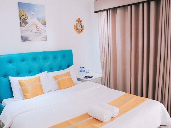 Une chambre d’hôtel avec une tête de lit bleue, du linge de lit blanc et un tableau représentant un voilier accroché au mur.