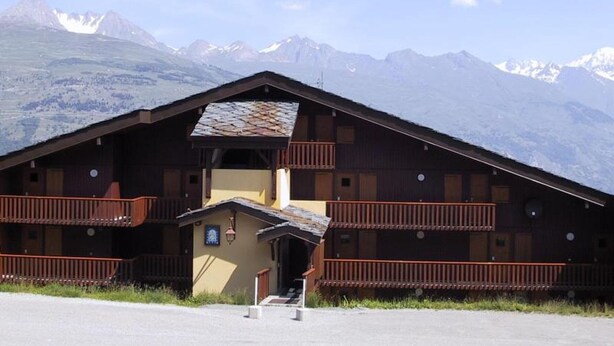 Un chalet en bois doté d’un balcon, d’un petit hall d’entrée et offrant une vue sur des montagnes enneigées.