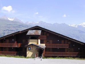 Una baita di legno con un balcone, un piccolo ingresso e vista sulle montagne innevate.