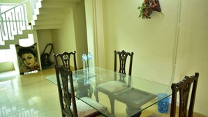 A dining area with a glass-top table and wooden chairs, a staircase in the background, and a wall-mounted plant. - AJK Guest House (Mekhtar)