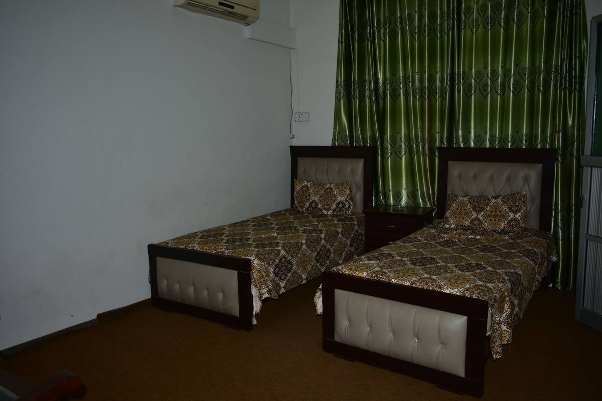 A bedroom with two single beds, a green curtain, and a white wall.