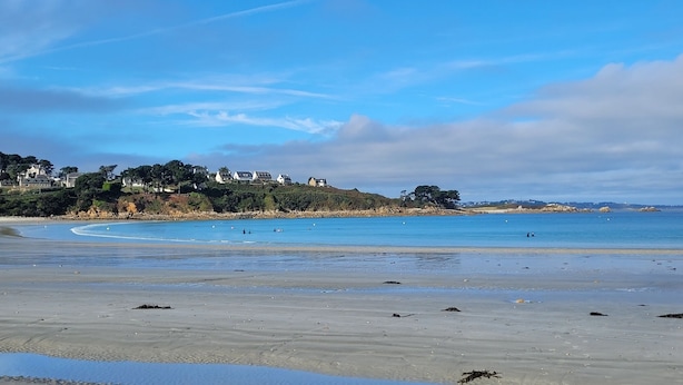A beach with clear blue water, a sandy shore, and houses in the background. - Maison Familiale Avec SPA Proche mer et Commodités (Trélévern)