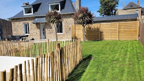 A stone house with a sloped roof, a wooden fence, and a well-maintained lawn. - Maison Familiale Avec SPA Proche mer et Commodités (Trélévern)