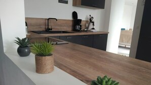 A modern kitchen with a wooden countertop, a sink, and a coffee maker. There are two potted plants on the counter. - Maison Familiale Avec SPA Proche mer et Commodités (Trélévern)