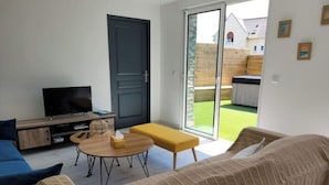 A modern living room with a sofa, a coffee table, a television, and a sliding glass door leading to a garden. - Maison Familiale Avec SPA Proche mer et Commodités (Trélévern)