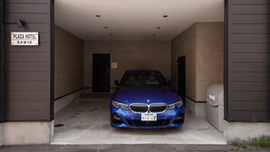 A blue BMW parked in a covered parking area of a building with a sign indicating "PLAZA HOTEL S4W12". - THE PLAZA HOTEL S4W12 (Sapporo)