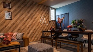 A cozy room with a wooden wall, a dining table with chairs, a sofa, and a small ottoman. - THE PLAZA HOTEL S4W12 (Sapporo)