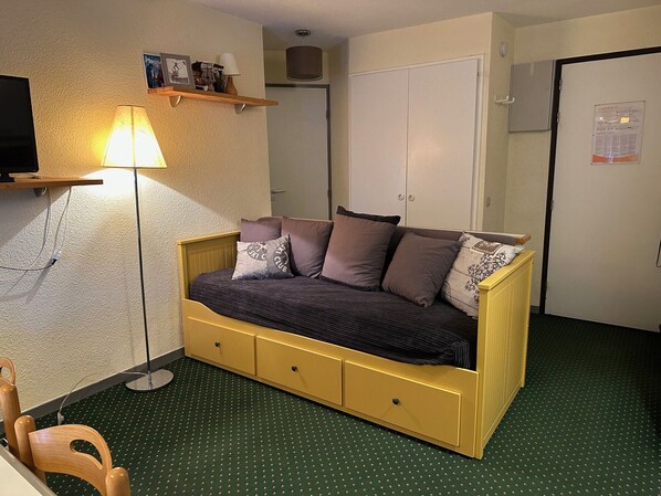 Una habitación pequeña con una cama individual, un escritorio, una silla, una lámpara y un armario.