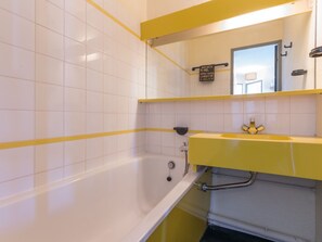 Un baño con paredes de azulejos blancos, un lavamanos amarillo y una bañera.